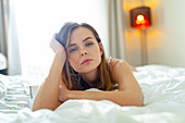 Porträt einer Frau auf dem Bett liegend und in die Kamera schauend zu Hause