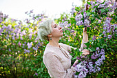 Portrait einer Frau, die an Fliederblüten im Garten riecht