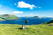 Wanderer steht auf einem Felsen und betrachtet den Fjord im Sommer, Nordradalur, Streymoy Island, Färöer Inseln, Dänemark, Europa