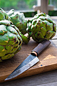 Fresh artichokes with knife on wooden cutting board
