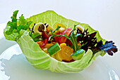 White cabbage leaf bowl with mixed vegetable salad and herbs