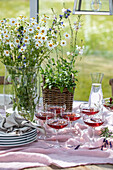 Wildflower bouquet with daisies in front of a laid table with aperitif glasses