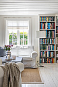 Helles Wohnzimmer im Landhausstil mit vollgepacktem Bücherregal und bequemem Sofa