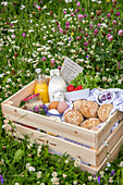 Frühstückskiste mit Eiern, Saft und Brötchen auf einer Blumenwiese