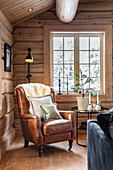 Comfortable leather armchair with fur and cushions in a rustic wooden house with a view of snow-covered trees