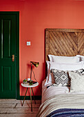 Schlafzimmer mit orangefarbener Wand, grüner Tür und rustikalem Holzkopfteil
