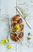 Osterzopf mit eingebackener Eierschale gefüllt mit Schlüsselblumen und Primel, mit Schnur auf Leinentuch gebunden, Blumendekoration