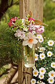 Frühlingsstrauß mit Narzisse (Narcissus), Kirschblütenzweig, Maiglöckchen (Convallaria majalis), Tulpen (Tulipa) und Sternmieren (Stellaria) in Vase an Pfosten hängend