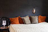 Bedroom with bed and decorative pillows in orange and brown against a black wall