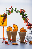 Orangenscheiben in Waffeltüten, Blütenzweig in Glasvase