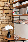 Shelf with books and designer lamp in front of a rustic stone wall