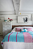 Schlafzimmer im Landhausstil mit Holzbett, gemusterter Bettwäsche und Wandbild