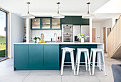 Modern kitchen with green-blue cabinets, white worktop and bar stools