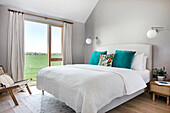 Bedroom with large windows, double bed and teal throw pillows