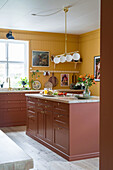 Kitchen with yellow wall, terracotta-colored cupboards and kitchen island