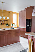 Kitchen in brick red and mustard yellow with a bouquet of flowers on the kitchen island