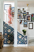 Staircase with floral wallpaper and family photos on a white wooden wall