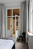 Bedroom with light grey curtains, open door and black chair