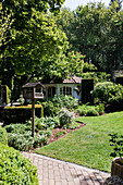 Romantic garden path with bird house and lush vegetation around a garden shed