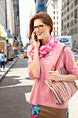 Fröhliche junge Frau mit Brille im rosa Pulli telefoniert auf der Straße