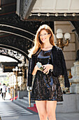 Junge Frau in schwarzem Minikleid mit Pailetten und Jäckchen steht auf der Straße