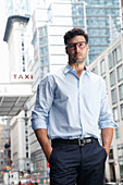 Junger Mann mit Brille in dunkler Anzugshose und hellem Hemd steht auf der Straße