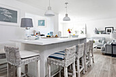 Bright kitchen with kitchen island and woven bar stools, open-plan living area in the background