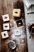 Top view on Linzer cookies with rhombus-shape holes on the wooden breadboard with jar of jam