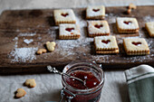 Jar of red berry jam with metal spoon with flower ornament with Linzer cookies as background
