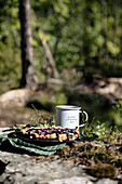 Bluew berry pie served on large stone with bluewberry leaves in forest close to white metal mug with slogan