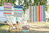 Striped towels on clothes line next to camping chair and camper