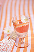 Glass with water, blossom and grapefruit slices on striped tablecloth