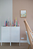 White cupboard with colorful candles and abstract picture on the wall