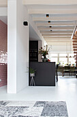 Modern kitchen with black cooking island and open-plan living area with white wooden beamed ceiling