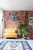 Yellow armchair in front of red brick wall with hanging bicycle and houseplants