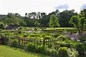 Cottage garden formally laid out inside wooden fence with vegetables and flowers