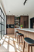 Kitchen with dark wooden fronts, cooking island and bar stools in front of floor-to-ceiling windows