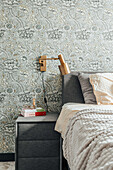 Upholstered bed with patterned wallpaper and golden bedside lamp in the bedroom