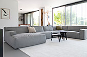 Grey corner sofa and round side tables in modern living room with large window front