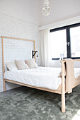 Bright bedroom with light-coloured wooden bed in front of a white brick wall