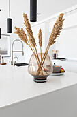 Large glass vase with dried millet on a white kitchen island