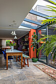 Dining area with glass roof, long wooden table, colourful chairs and bench seat