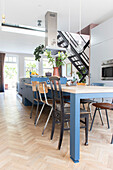 Open-plan kitchen with blue elements and industrial-style chairs