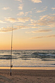 Fishing pole in sand on tranquil ocean beach at sunset, Bat Yam, Israel\n