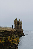 Tourist auf einer Klippe bei einer Burgruine über dem Meer, Keiss, Schottische Highlands, Schottland