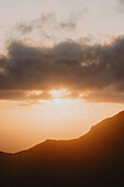 Sunset in clouds over silhouetted land, Klakkur, Klaksvik, Faroe Islands\n
