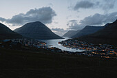 Illuminated town and silhouetted hills at dusk, Klakkur, Klaksvik, Faroe Islands\n