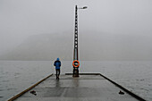 Mann steht im Regen auf dem Steg über dem nebligen Meer, Kollafjorour, Färöer Inseln