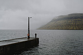 Man on jetty looking at foggy ocean seascape, Kollafjorour, Faroe Islands\n