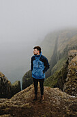 Mann in Jacke wandert auf schroffen Klippen, Dunnesdrangar, Vagar, Färöer Inseln